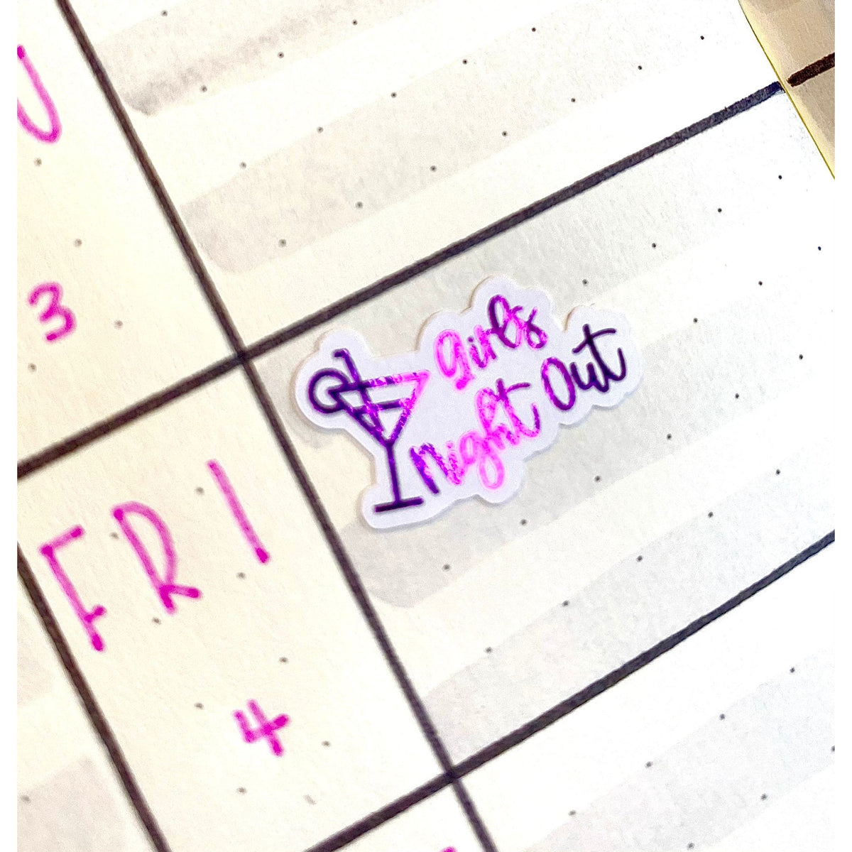 Pink and purple foiled script planner sticker with a cocktail glass design, displayed on a monthly planner page.